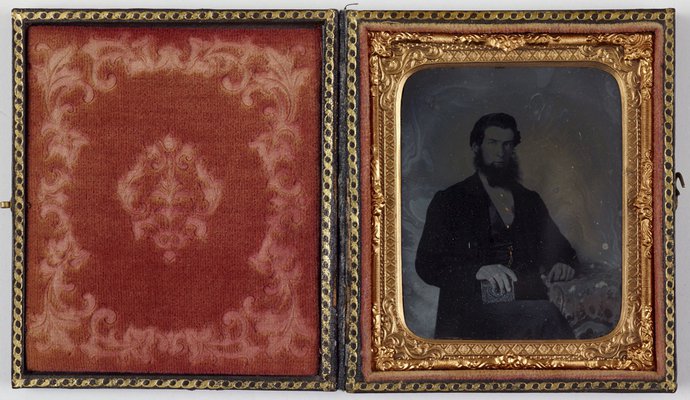 Alternate image of Untitled (unknown man with dark hair and beard, gold watch chain, rings and shirt studs, holding an ambrotype? with Ottoman embroidered table cloth) by Unknown